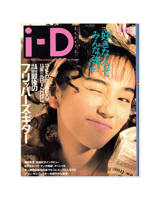 A magazine cover featuring a close-up portrait of a woman with wavy dark hair, wearing a patterned headband and holding a newspaper. Large pink and blue text includes 'i-D' and Japanese copy.