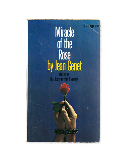 Book cover of 'Miracle of the Rose' by Jean Genet with a hand holding a rose against a blue background.
